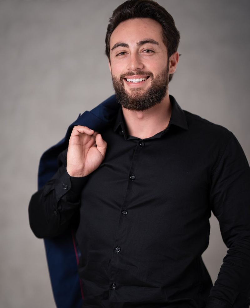 Dr. Guilherme Augusto de camisa preta, sorrindo, com o paletó apoiado no ombro